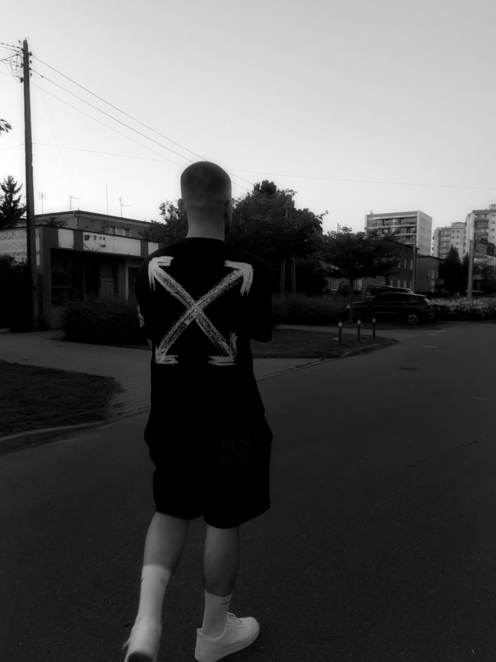 Kacper Graś (Mysteryu) sfotografowany od tyłu na osiedlowej ulicy, w czarnej koszulce z białym znakiem X - czarno-białe zdjęcie